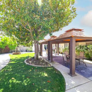 A beautiful outdoor space featuring a well-maintained garden with trees and a shaded patio area.