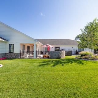 A spacious backyard with a well-maintained lawn, patio area, and trees under a clear blue sky.