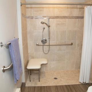 An accessible shower with a foldable chair and grab bars for support.