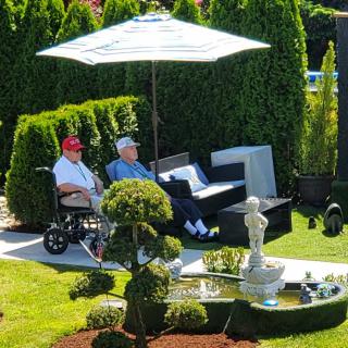 Two people relax in a beautifully landscaped garden with a fountain and an umbrella providing shade.