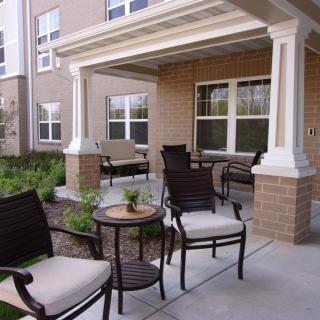 A cozy outdoor patio with seating and a small table, set against a building with large windows.