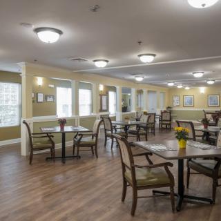 A well-lit dining area with neatly arranged tables and chairs on a wooden floor.