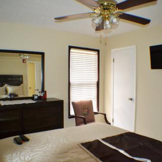 A cozy bedroom featuring a large bed, dresser with a mirror, ceiling fan, and wall-mounted TV.