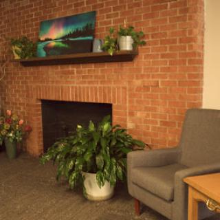 A cozy living room corner featuring a brick wall, a fireplace, potted plants, and a comfortable gray chair.