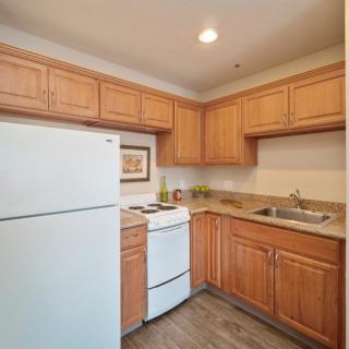 A small kitchen with wooden cabinets, a refrigerator, stove, and sink.