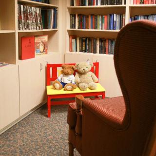 A cozy library corner with teddy bears on a small red bench surrounded by shelves of books.