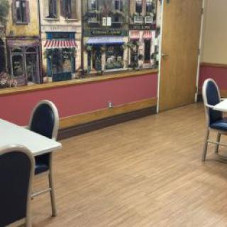 A dining area with several tables and chairs, featuring a wall mural depicting a street scene.