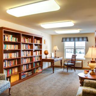 A cozy library room with a bookshelf, desk, and comfortable seating.