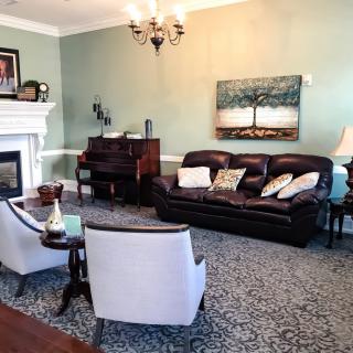 A cozy living room featuring a leather sofa, two armchairs, and a piano, accented by a fireplace and artwork on the wall.
