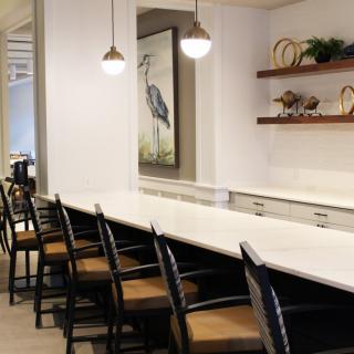 Modern kitchen with a long countertop and seating area, accented by pendant lights and decorative shelves.