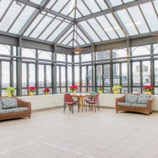 A spacious conservatory with a glass ceiling, featuring comfortable seating and colorful potted plants.