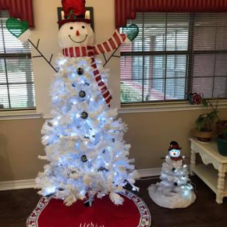 A whimsical Christmas display featuring a white Christmas tree designed like a snowman, complete with lights and festive decorations.