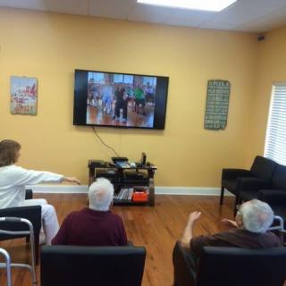 Seniors participating in a group exercise session while watching a program on television.