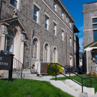 A historic stone building with arched windows and a grassy lawn under a clear blue sky.