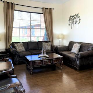 A cozy living room featuring dark leather sofas, a wooden coffee table, and soft natural light filtering through the curtains.