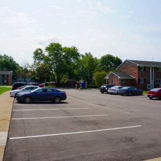 A parking lot with several cars parked, surrounded by trees and buildings on a clear day.