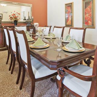 An elegant dining room with a large wooden dining table, neatly set with green napkins and glassware.