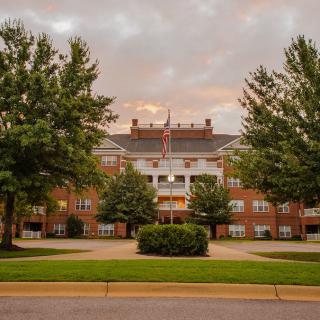 A symmetrical brick building with an American flag, framed by trees under a cloudy sky.