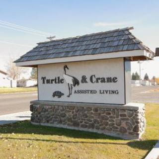 A roadside sign for Turtle & Crane Assisted Living, featuring a stone base and wooden roof.