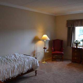 A cozy bedroom with a single bed, standing lamp, and armchair near a window.
