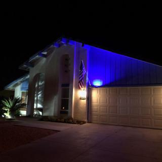 A modern house illuminated with blue lights at night, featuring an American flag.