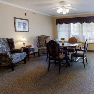 A cozy living room with a dining table and chairs, a lamp, and comfortable armchairs, decorated with artwork on the wall.