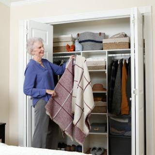 An elderly woman smiles while organizing her closet with a cozy blanket.