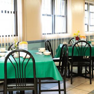 A neatly arranged dining area with tables covered in green tablecloths, ready for guests.