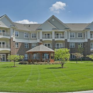 A residential apartment building with a well-maintained lawn and a gazebo under a clear sky.