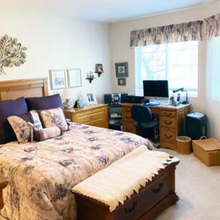 A cozy bedroom with a wooden bed and a computer desk by the window.