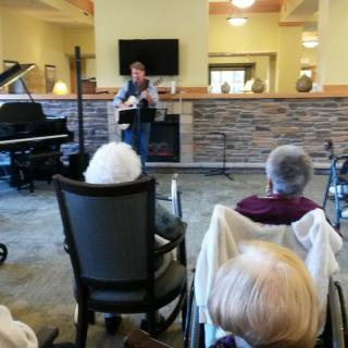 A musician performs in front of an elderly audience at an indoor venue.