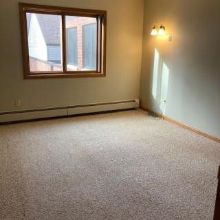 An empty room with a carpeted floor, featuring a window and wall lamp.