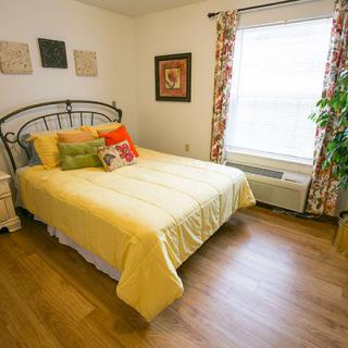 A cozy bedroom with a yellow bedspread, colorful pillows, and a large window letting in natural light.