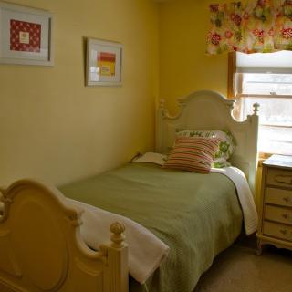 A cozy bedroom with a single bed, yellow walls, and colorful decor.