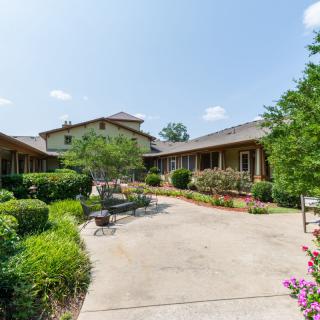 A scenic courtyard with lush greenery, benches, and a central pathway leading to a building.