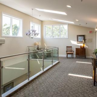 A well-lit hallway with glass railings, a chandelier, and stylish furnishings.