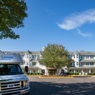 A white multi-story building with a parked van in front, surrounded by trees and under a clear blue sky.