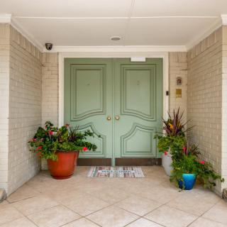 A welcoming entrance with a green double front door and potted plants on either side.