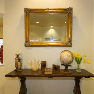 A vintage-style hallway setup with a framed mirror, decorative table, globe, and vase of flowers.