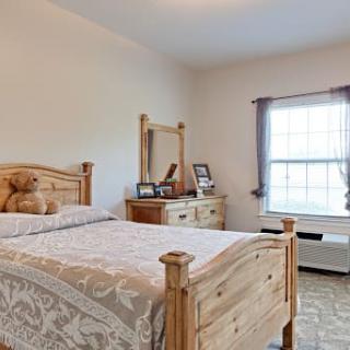A cozy bedroom with wooden furniture, featuring a bed, dresser with mirror, and a window letting in natural light.