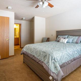 A cozy bedroom with a large bed, ceiling fan, and carpeted floor.