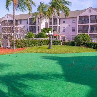 A sunny day view of an apartment complex with a putting green surrounded by palm trees.