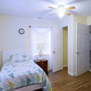 A cozy bedroom with a single bed, lamp, and a ceiling fan.