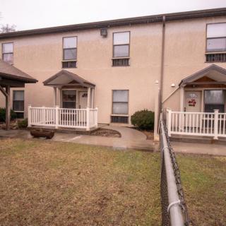 Exterior view of a residential apartment building with porches and a fenced lawn.