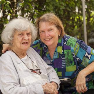 A middle-aged woman and an elderly woman smiling together outdoors.