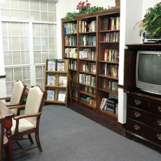 A cozy library corner with bookshelves, a reading table with chairs, and an old television.