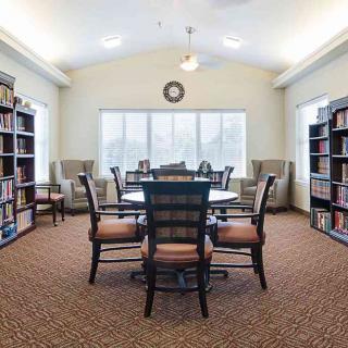 A cozy library with bookshelves, a central table, and chairs arranged for reading.