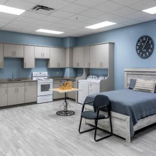 A modern studio room featuring a kitchenette, bed, and simple furnishings.