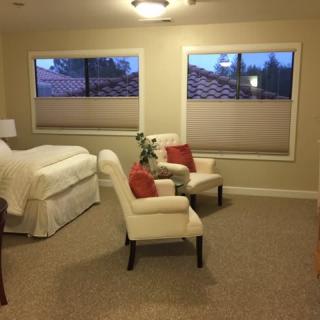 A cozy bedroom with a neatly made bed, two armchairs, and large windows.
