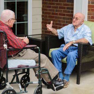 Two elderly men having a conversation outside, one sitting in a wheelchair.